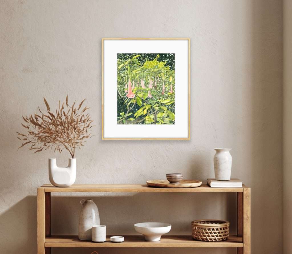 large highly detailed intimate landscape watercolor painting of Angel’s Trumpet (Brugmansia) in light pine frame with white matting shown hanging over blond wood bookcase full of baskets and pottery on a stucco wall